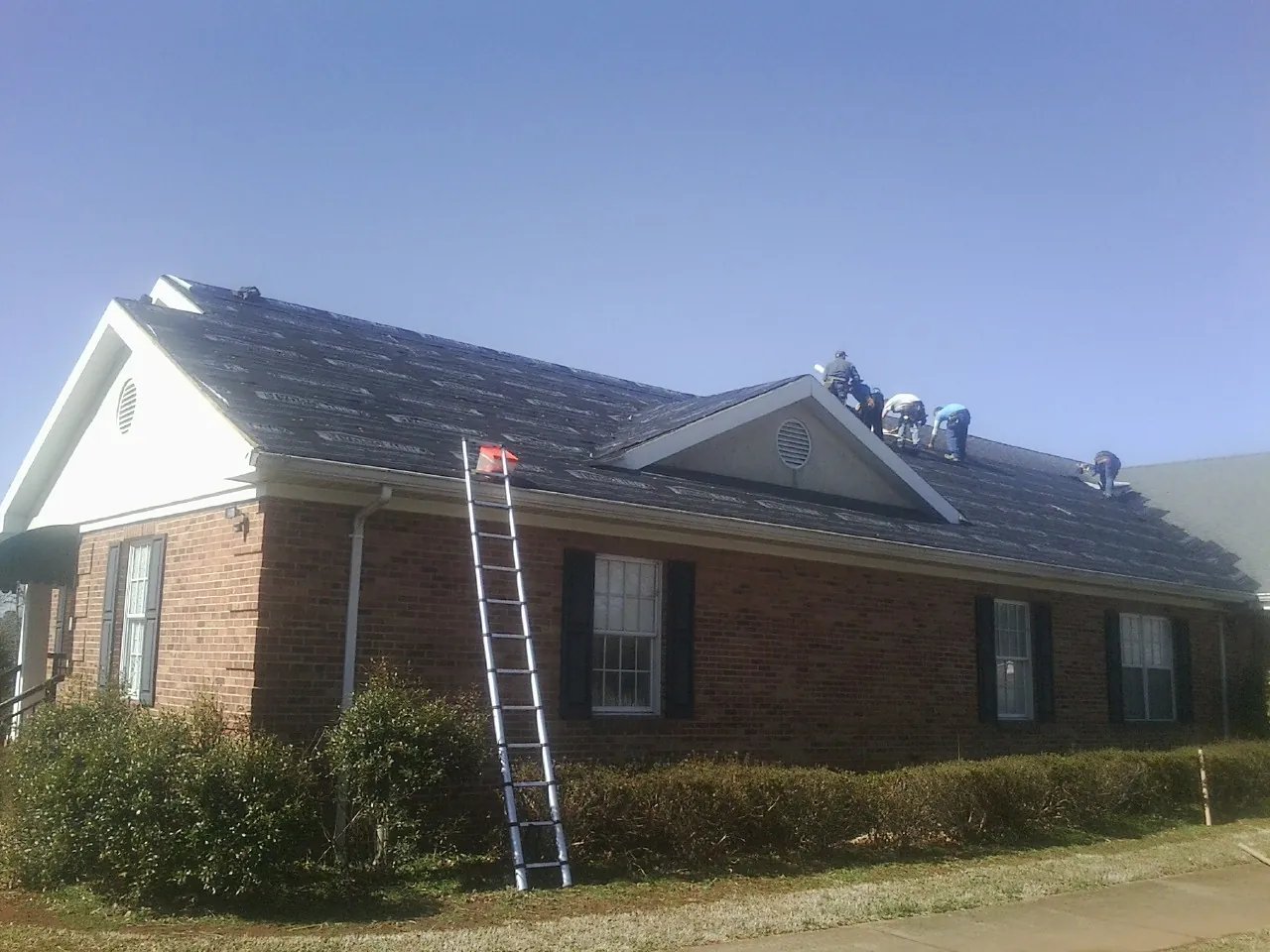 Crew tearing shingles off a brick ranch roof with a ladder set — Metal Roof Repair work by our crew in Oak Park