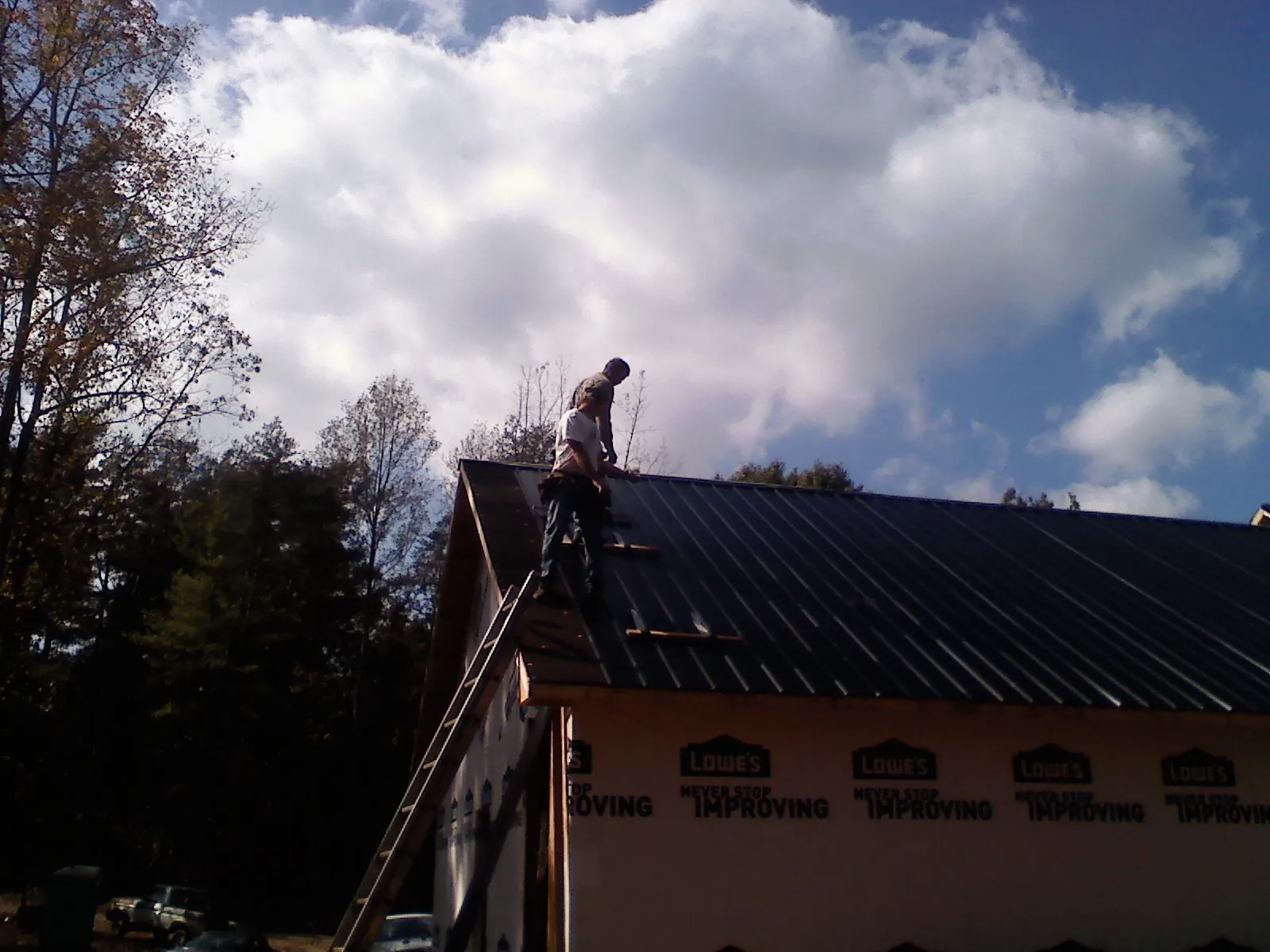 Roofer fastening dark metal panels high against a cloudy sky, from a Roof Inspection job in Oak Park